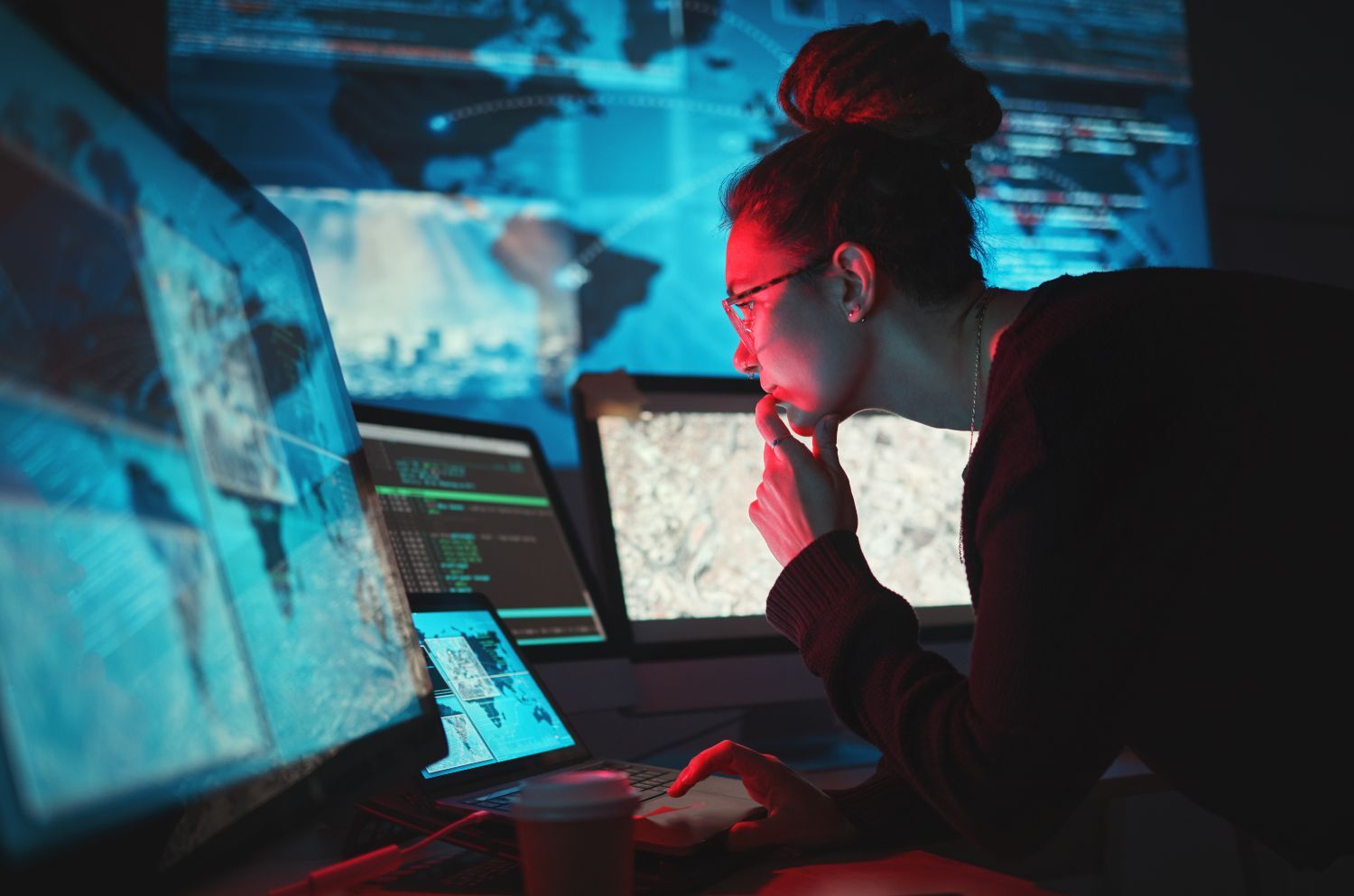woman looks at computer screens with world maps in a cybersecurity situation room
